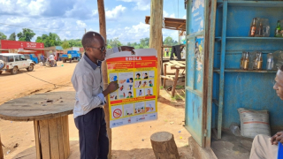 Legenda: Um promotor de saúde de MSF conversa com um comerciante em Madudu, próximo ao epicentro do surto de Ebola em Uganda. Sam Taylor/MSF, 2022.